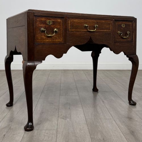 fig 7. An 18th-century Georgian oak side table featuring three drawers with brass drop handles, an arched apron, and cabriole legs.