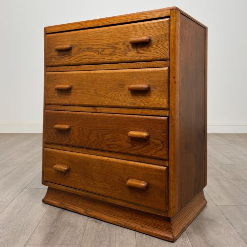 fig 1. A vintage medium-toned oak chest of drawers featuring four graduated drawers with matching wooden bar handles set on a flared plinth base.