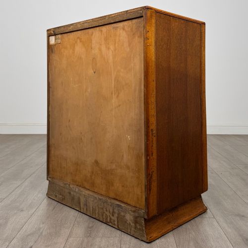 fig 5. A vintage medium-toned oak chest of drawers featuring four graduated drawers with matching wooden bar handles set on a flared plinth base.