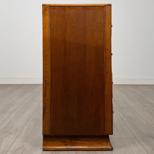 fig 6. A vintage medium-toned oak chest of drawers featuring four graduated drawers with matching wooden bar handles set on a flared plinth base.