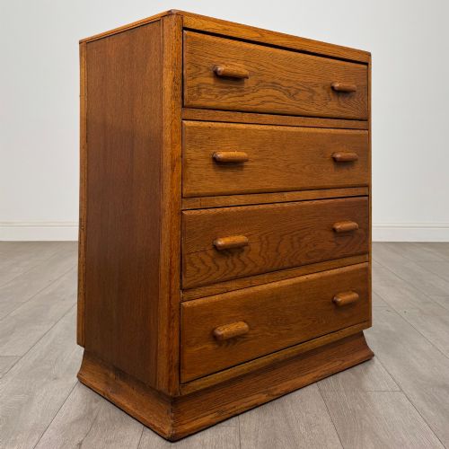 fig 7. A vintage medium-toned oak chest of drawers featuring four graduated drawers with matching wooden bar handles set on a flared plinth base.