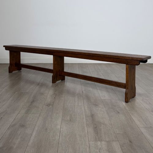 fig 1. A long 19th-century Georgian oak tavern bench featuring a smooth plank seat supported by three sturdy slab legs and a full-length lower stretcher.