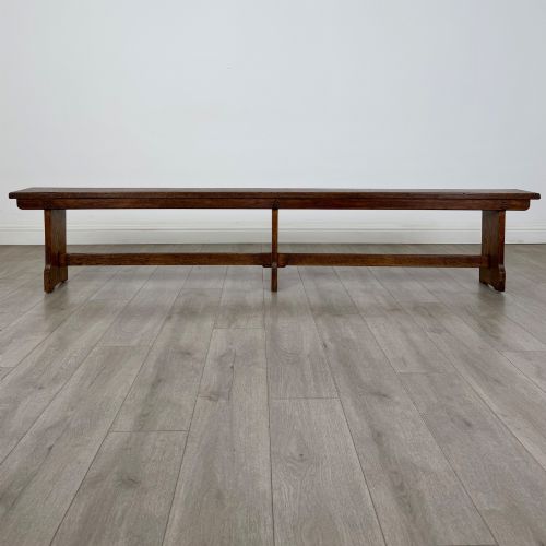 fig 4. A long 19th-century Georgian oak tavern bench featuring a smooth plank seat supported by three sturdy slab legs and a full-length lower stretcher.