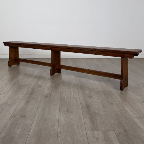fig 5. A long 19th-century Georgian oak tavern bench featuring a smooth plank seat supported by three sturdy slab legs and a full-length lower stretcher.