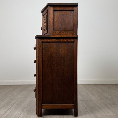 fig 3. An Edwardian dark oak cupboard featuring an upper canted cabinet with carved decorative panels above four graduated drawers with turned wooden knobs.