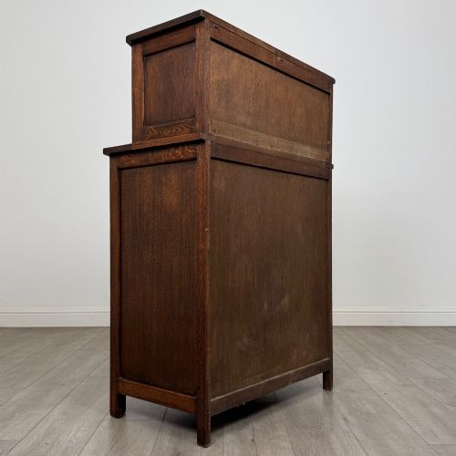 fig 4. An Edwardian dark oak cupboard featuring an upper canted cabinet with carved decorative panels above four graduated drawers with turned wooden knobs.