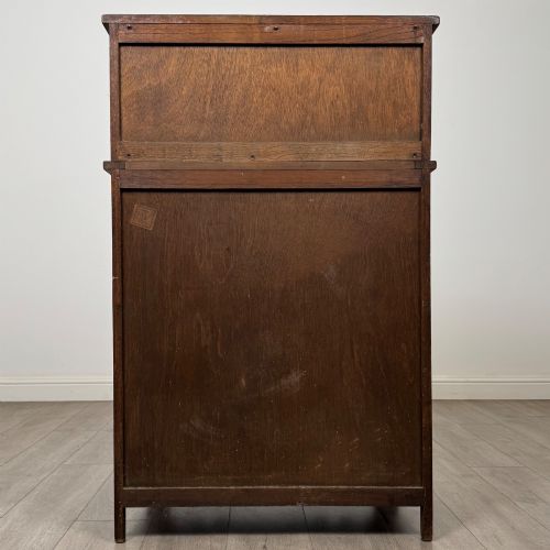 fig 5. An Edwardian dark oak cupboard featuring an upper canted cabinet with carved decorative panels above four graduated drawers with turned wooden knobs.