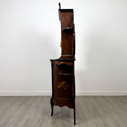 fig 3. A late 19th-century mahogany display cabinet featuring floral marquetry inlay, glazed central doors, oval side mirrors, and a decorative asymmetric crest pediment.