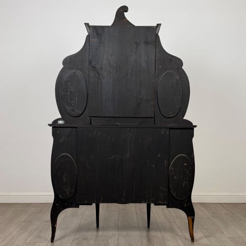 fig 5. A late 19th-century mahogany display cabinet featuring floral marquetry inlay, glazed central doors, oval side mirrors, and a decorative asymmetric crest pediment.