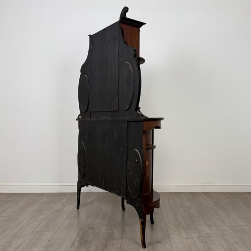 fig 6. A late 19th-century mahogany display cabinet featuring floral marquetry inlay, glazed central doors, oval side mirrors, and a decorative asymmetric crest pediment.