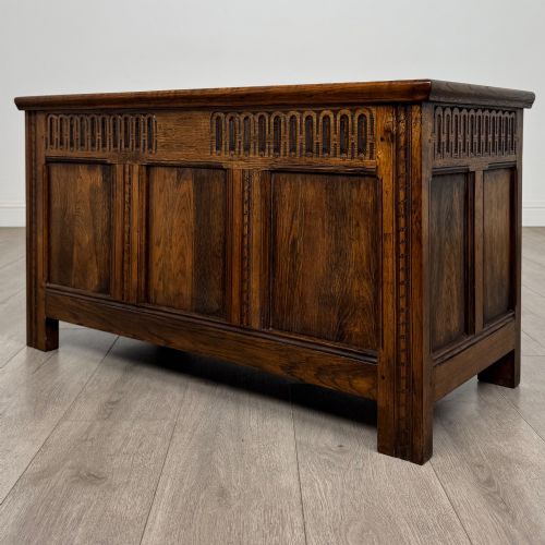 fig 1. A rectangular dark oak blanket box featuring a hinged top lid, panelled front sections, and carved arch motifs along the upper frieze.