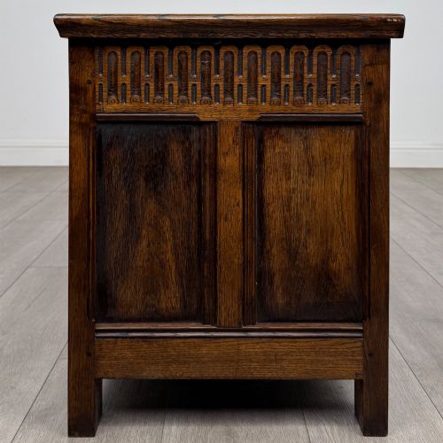 fig 2. A rectangular dark oak blanket box featuring a hinged top lid, panelled front sections, and carved arch motifs along the upper frieze.