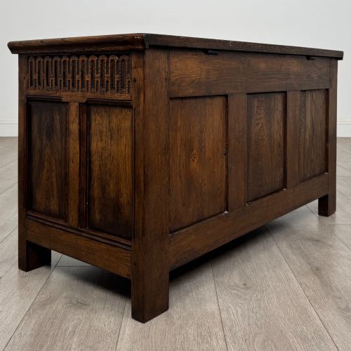 fig 3. A rectangular dark oak blanket box featuring a hinged top lid, panelled front sections, and carved arch motifs along the upper frieze.