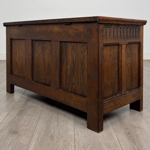 fig 5. A rectangular dark oak blanket box featuring a hinged top lid, panelled front sections, and carved arch motifs along the upper frieze.