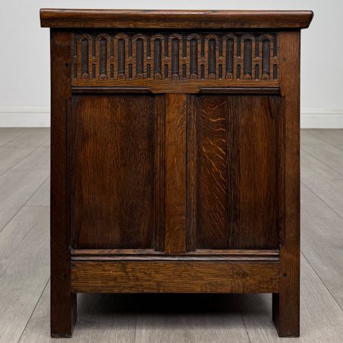 fig 6. A rectangular dark oak blanket box featuring a hinged top lid, panelled front sections, and carved arch motifs along the upper frieze.