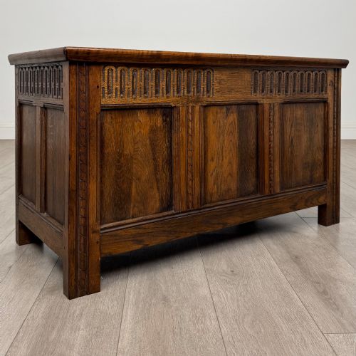 fig 7. A rectangular dark oak blanket box featuring a hinged top lid, panelled front sections, and carved arch motifs along the upper frieze.