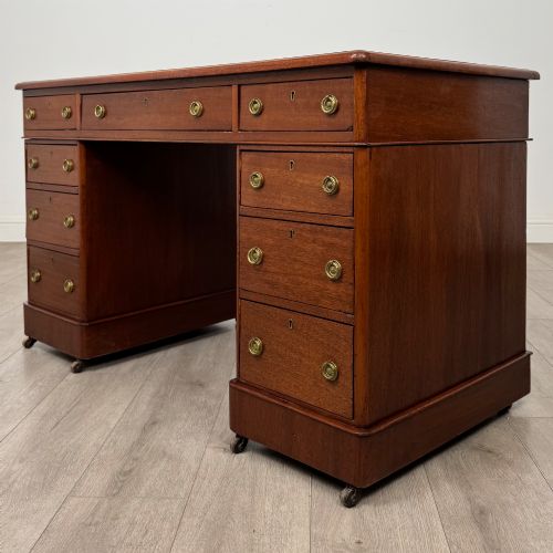 fig 1. A 19th-century Victorian mahogany pedestal desk featuring nine drawers with circular brass knobs and keyholes, supported by twin plinth bases on casters.