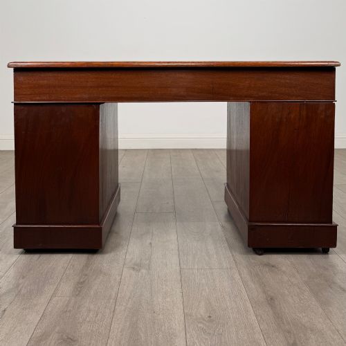 fig 4. A 19th-century Victorian mahogany pedestal desk featuring nine drawers with circular brass knobs and keyholes, supported by twin plinth bases on casters.
