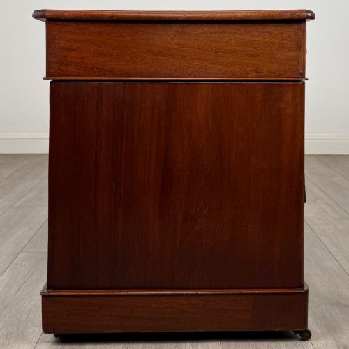 fig 6. A 19th-century Victorian mahogany pedestal desk featuring nine drawers with circular brass knobs and keyholes, supported by twin plinth bases on casters.