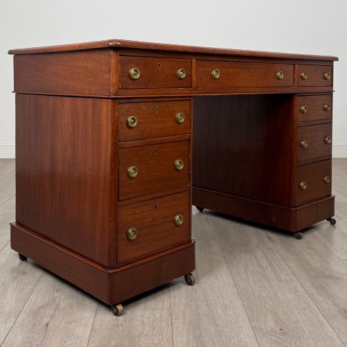fig 7. A 19th-century Victorian mahogany pedestal desk featuring nine drawers with circular brass knobs and keyholes, supported by twin plinth bases on casters.