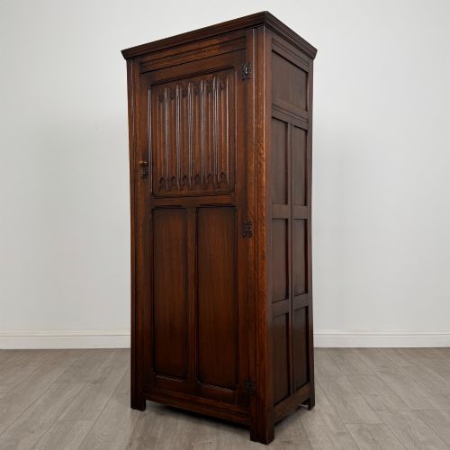 fig 2. A tall single-door dark oak Edwardian wardrobe featuring a carved upper linenfold panel and decorative iron hinges.