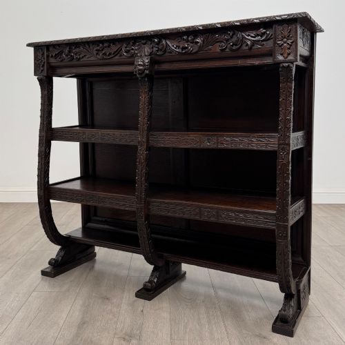 fig 1. A 19th-century dark oak open bookcase featuring hand-carved frieze foliage, a central mask motif, and three tiers of open shelving.