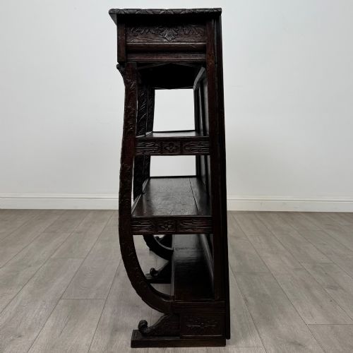 fig 2. A 19th-century dark oak open bookcase featuring hand-carved frieze foliage, a central mask motif, and three tiers of open shelving.