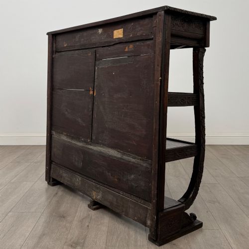 fig 5. A 19th-century dark oak open bookcase featuring hand-carved frieze foliage, a central mask motif, and three tiers of open shelving.