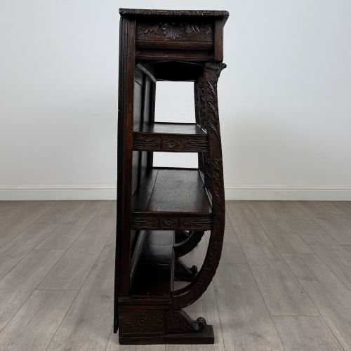 fig 6. A 19th-century dark oak open bookcase featuring hand-carved frieze foliage, a central mask motif, and three tiers of open shelving.