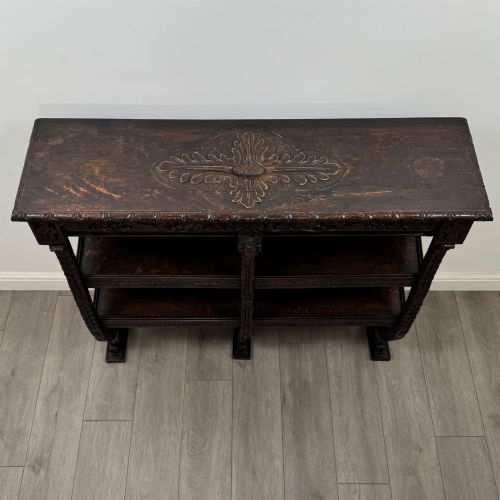 fig 8. A 19th-century dark oak open bookcase featuring hand-carved frieze foliage, a central mask motif, and three tiers of open shelving.