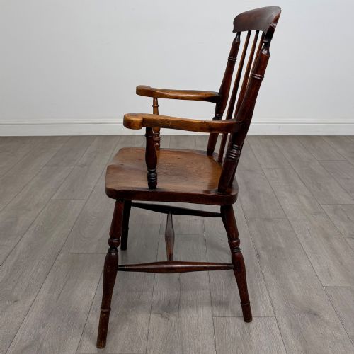 fig 1. An antique 19th-century oak stick back armchair featuring turned spindle backrests, curved wooden armrests, a contoured solid seat, and turned legs joined by stretchers.