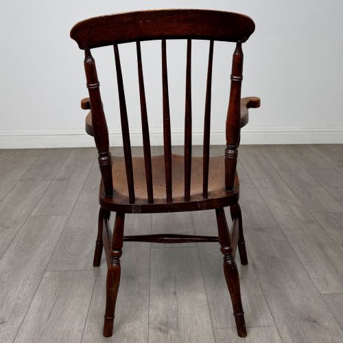 fig 3. An antique 19th-century oak stick back armchair featuring turned spindle backrests, curved wooden armrests, a contoured solid seat, and turned legs joined by stretchers.