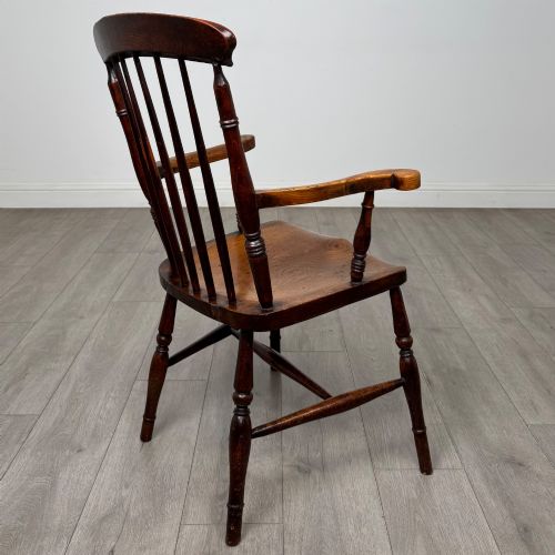 fig 4. An antique 19th-century oak stick back armchair featuring turned spindle backrests, curved wooden armrests, a contoured solid seat, and turned legs joined by stretchers.