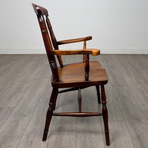 fig 5. An antique 19th-century oak stick back armchair featuring turned spindle backrests, curved wooden armrests, a contoured solid seat, and turned legs joined by stretchers.