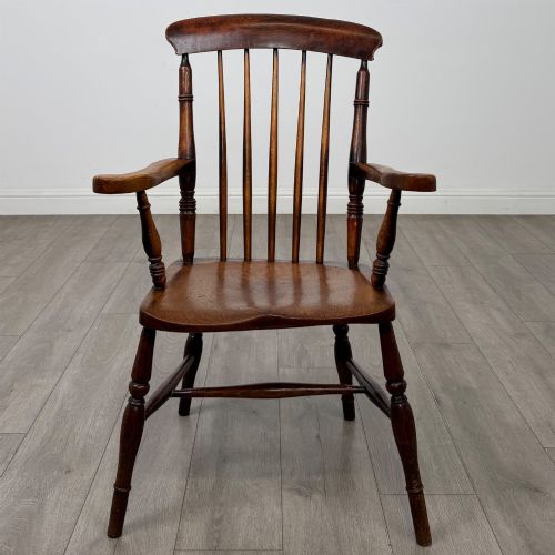 fig 7. An antique 19th-century oak stick back armchair featuring turned spindle backrests, curved wooden armrests, a contoured solid seat, and turned legs joined by stretchers.