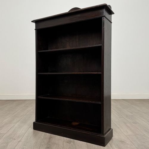 fig 2. An Edwardian dark-stained oak open bookcase featuring four shelf tiers containing red leather-bound books against a white background.