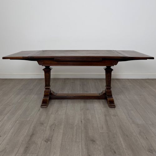fig 1. An Edwardian dark oak draw leaf dining table featuring extended side leaves, carved pedestal supports, and a low connecting stretcher.