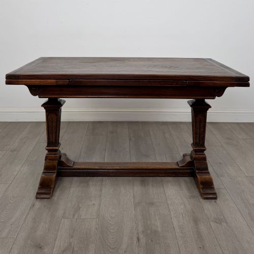 fig 2. An Edwardian dark oak draw leaf dining table featuring extended side leaves, carved pedestal supports, and a low connecting stretcher.