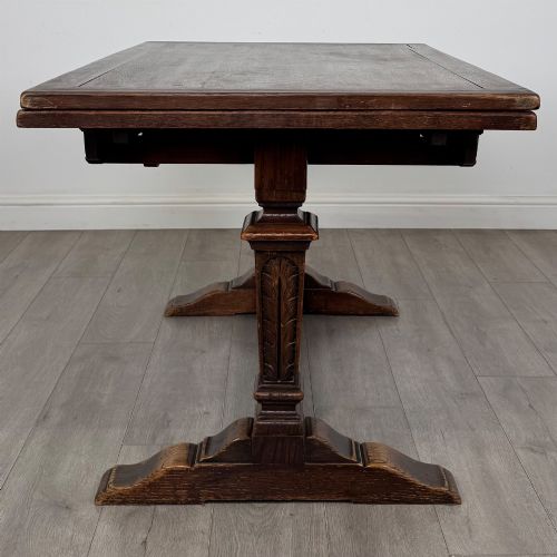 fig 3. An Edwardian dark oak draw leaf dining table featuring extended side leaves, carved pedestal supports, and a low connecting stretcher.