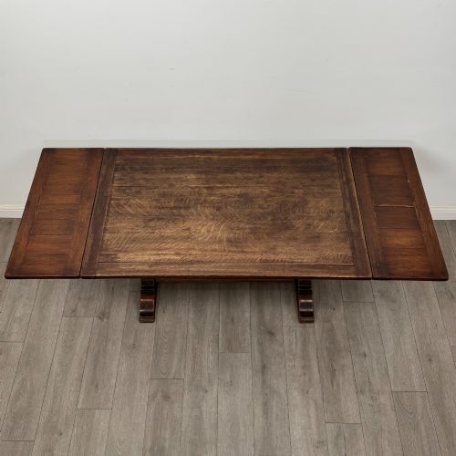 fig 5. An Edwardian dark oak draw leaf dining table featuring extended side leaves, carved pedestal supports, and a low connecting stretcher.