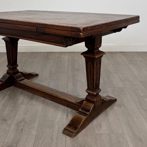 fig 6. An Edwardian dark oak draw leaf dining table featuring extended side leaves, carved pedestal supports, and a low connecting stretcher.