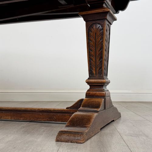 fig 7. An Edwardian dark oak draw leaf dining table featuring extended side leaves, carved pedestal supports, and a low connecting stretcher.
