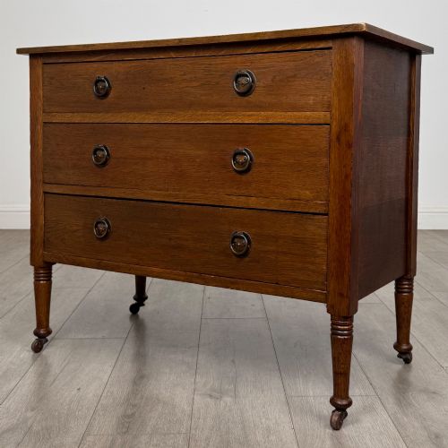 fig 1. An antique Edwardian oak chest featuring three full-width drawers with brass ring drop handles, set on turned legs with castors.