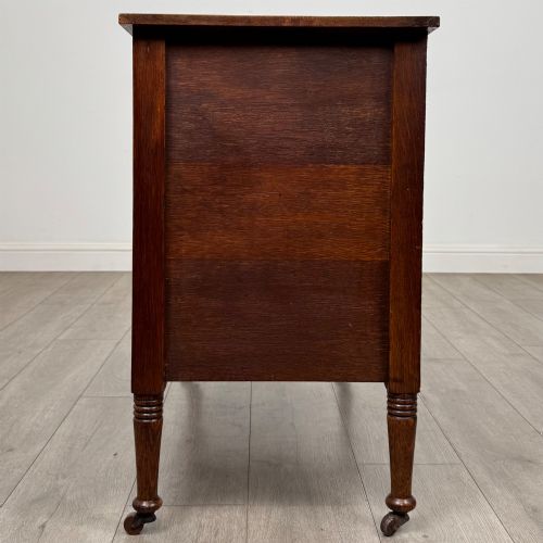 fig 2. An antique Edwardian oak chest featuring three full-width drawers with brass ring drop handles, set on turned legs with castors.