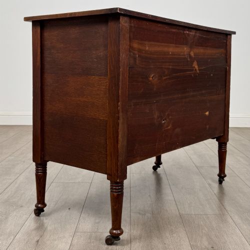 fig 3. An antique Edwardian oak chest featuring three full-width drawers with brass ring drop handles, set on turned legs with castors.
