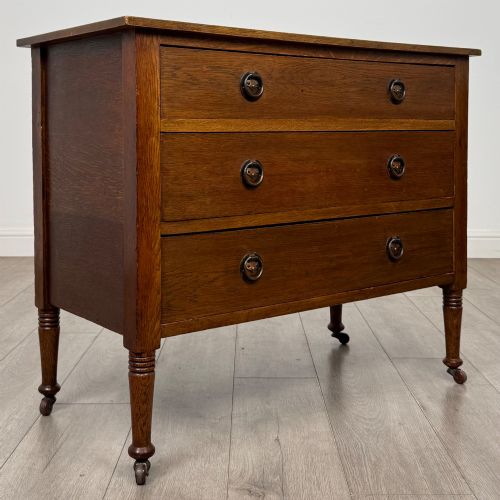 fig 7. An antique Edwardian oak chest featuring three full-width drawers with brass ring drop handles, set on turned legs with castors.