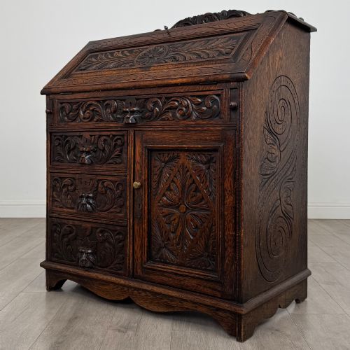 fig 2. A dark oak Victorian slant-front bureau featuring carved Green Man drawer pulls, foliage relief carvings, and a single panelled cupboard door.
