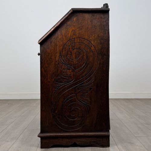 fig 3. A dark oak Victorian slant-front bureau featuring carved Green Man drawer pulls, foliage relief carvings, and a single panelled cupboard door.