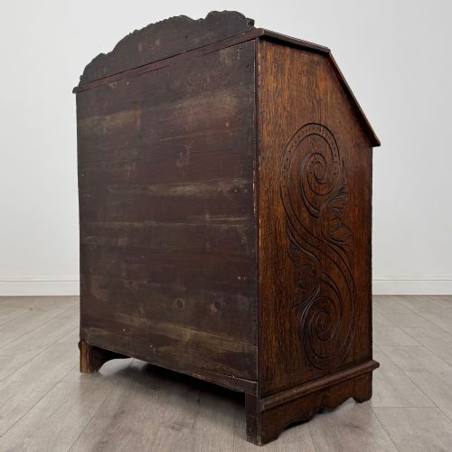fig 6. A dark oak Victorian slant-front bureau featuring carved Green Man drawer pulls, foliage relief carvings, and a single panelled cupboard door.
