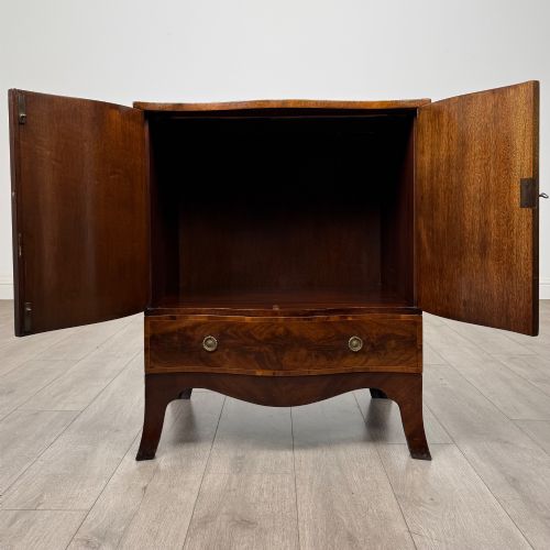 fig 1. A 20th-century mahogany serpentine cupboard featuring flame mahogany oval door panels, chevron veneering, a lower drawer with brass ring handles, and splayed bracket feet.